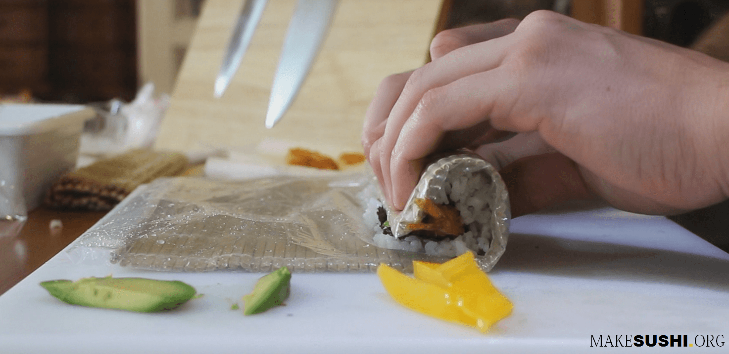 Rolling A Sushi Roll With A Bamboo Mat In A Plastic Bag